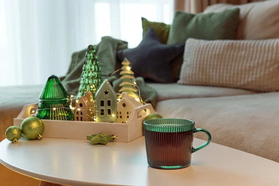 Jeune femme souriante en pull tricoté beige et bleu se reposant contre un radiateur à ailettes métalliques blanc dans un intérieur domestique